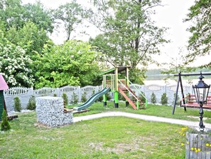 Playful fun awaits at this playground, featuring a wooden play structure with a slide and stairs, surrounded by lush greenery.