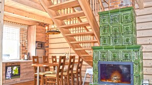 A wooden interior with a staircase, a dining area with chairs, and a green tiled fireplace. - Holiday Home by Lake in Nowa Wioska (Lubrza)