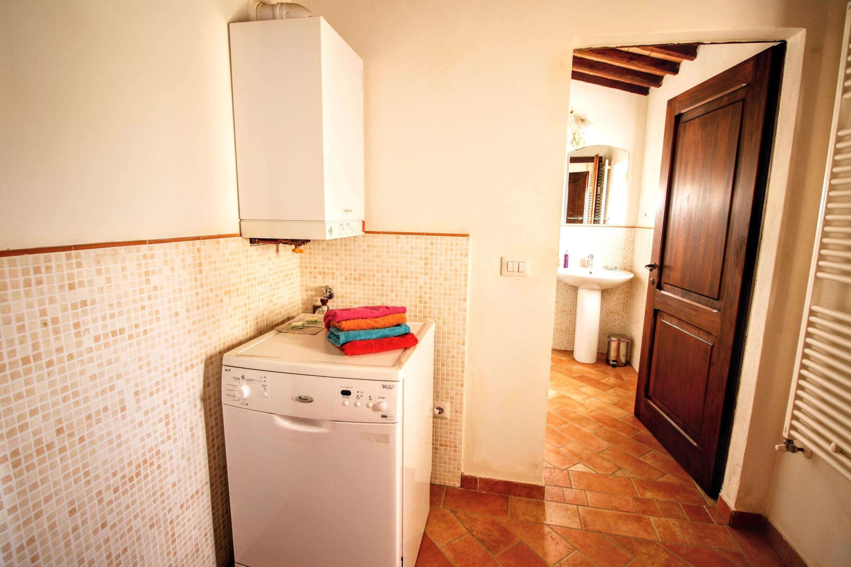 Una cocina compacta con lavadora, salpicadero de azulejos, lavabo y puerta de madera.