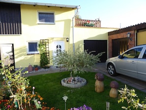 A residential building with a garage, a car parked in front, and a well-maintained garden with various plants and a decorative rabbit statue.
