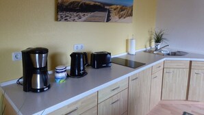 A kitchen with a coffee maker, a kettle, and a toaster on the counter. There is a painting on the wall above the counter. - Ferienhaus mit Balkon und Garten in Zweedorf (Bastorf)