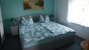 A bedroom with a bed, two bedside tables with lamps, a painting on the wall, and a window with curtains. - Ferienhaus mit Balkon und Garten in Zweedorf (Bastorf)