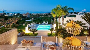 Ein Esszimmer mit Tisch, gedeckt für eine Mahlzeit, mit Blick auf einen Pool, Sitzgelegenheiten im Freien und einer Obstschale.