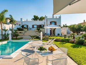 A poolside area with lounge chairs and a table, a staircase leading to a building, and a well-maintained garden. - Belvilla by OYO La Pigna Bianca (Misiliscemi)