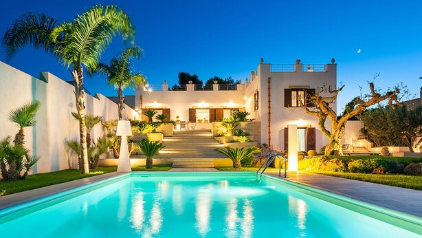 Ein modernes Haus mit Swimmingpool, einer Treppe zum Eingang und einer gut beleuchteten Fassade im Abenddämmerung.