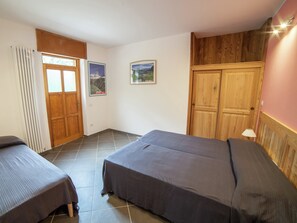 A bedroom with two beds, a radiator, wooden wardrobe, and two framed pictures on the wall.