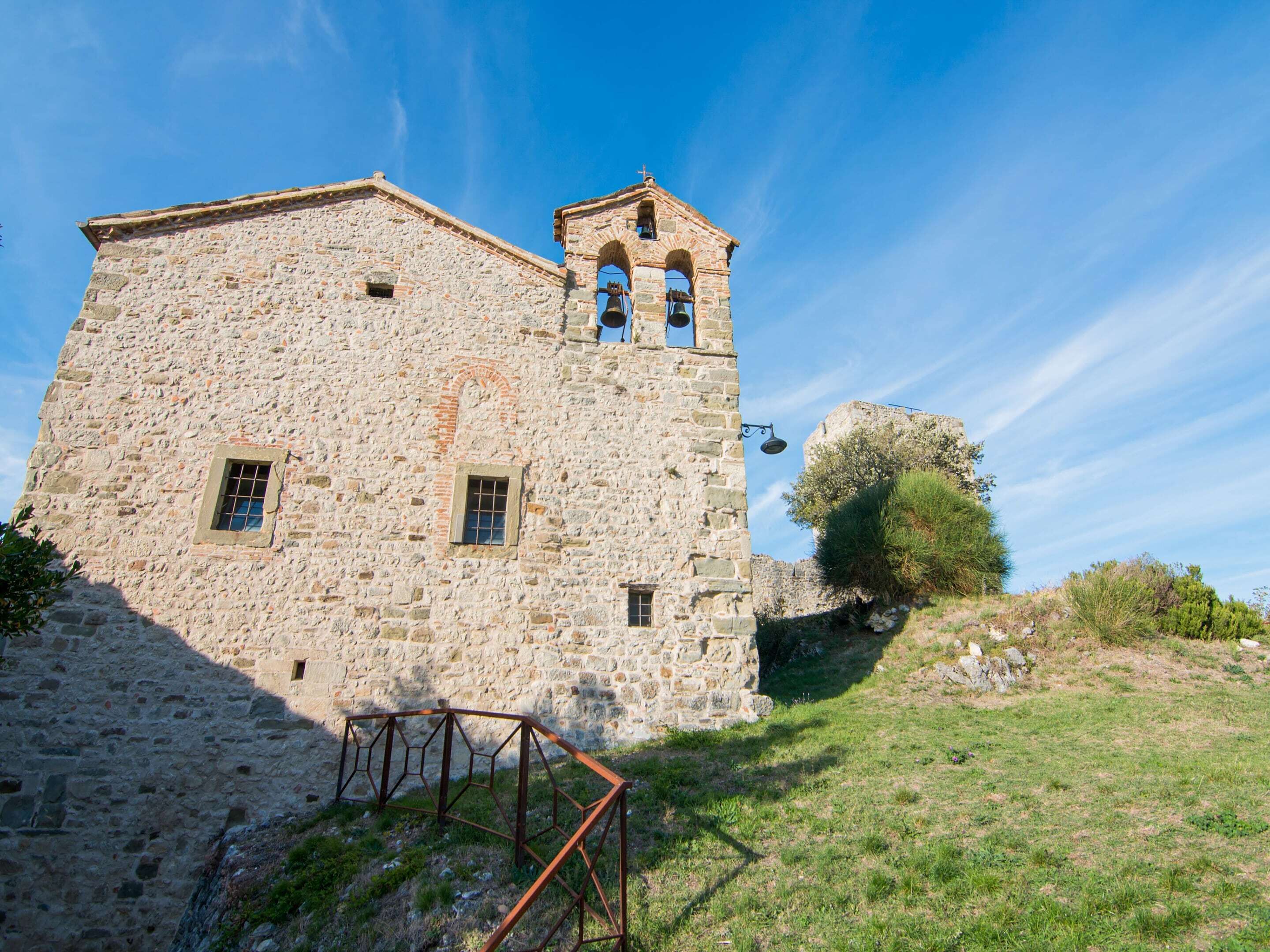 A stone building with a bell tower, a window, and a metal gate.