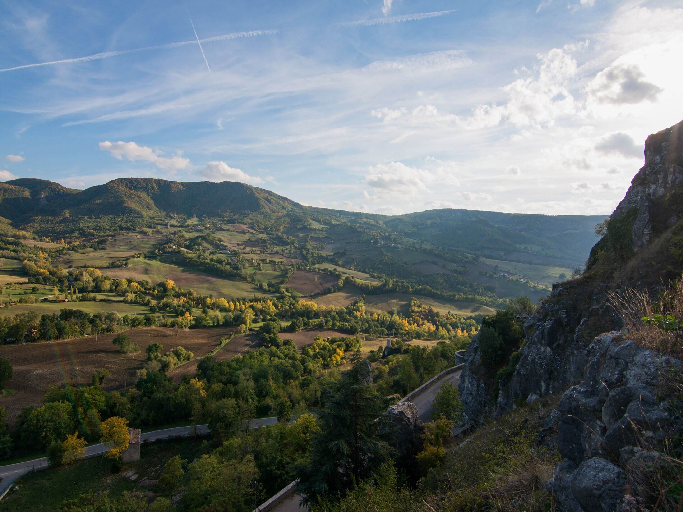 Vista panoràmica d'una vall amb turons ondulats, un camí sinuós i un penya-segat rocos a la dreta.