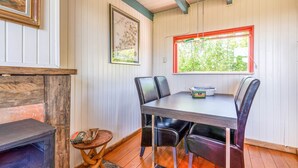 A dining area with a table, chairs, a window with a red frame, and a wall-mounted picture.