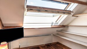 A room with a skylight, a television, a radiator, wooden flooring, and a striped lamp.
