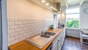 A modern kitchen with white subway tiles, a stainless steel sink, and a window with a view of greenery.