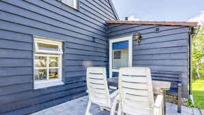 A patio with two white chairs and a table, a window, and a door with a blue awning.