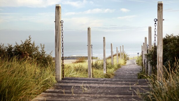 A wooden boardwalk leading to a beach with wooden posts and chains.