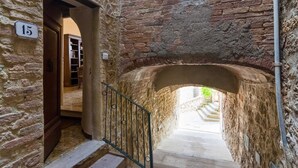 A narrow stone corridor with a staircase leading to a brighter area. A door labeled '15' is visible on the left. - Cozy 2-bedroom Apartment (Castelnuovo di Val di Cecina)
