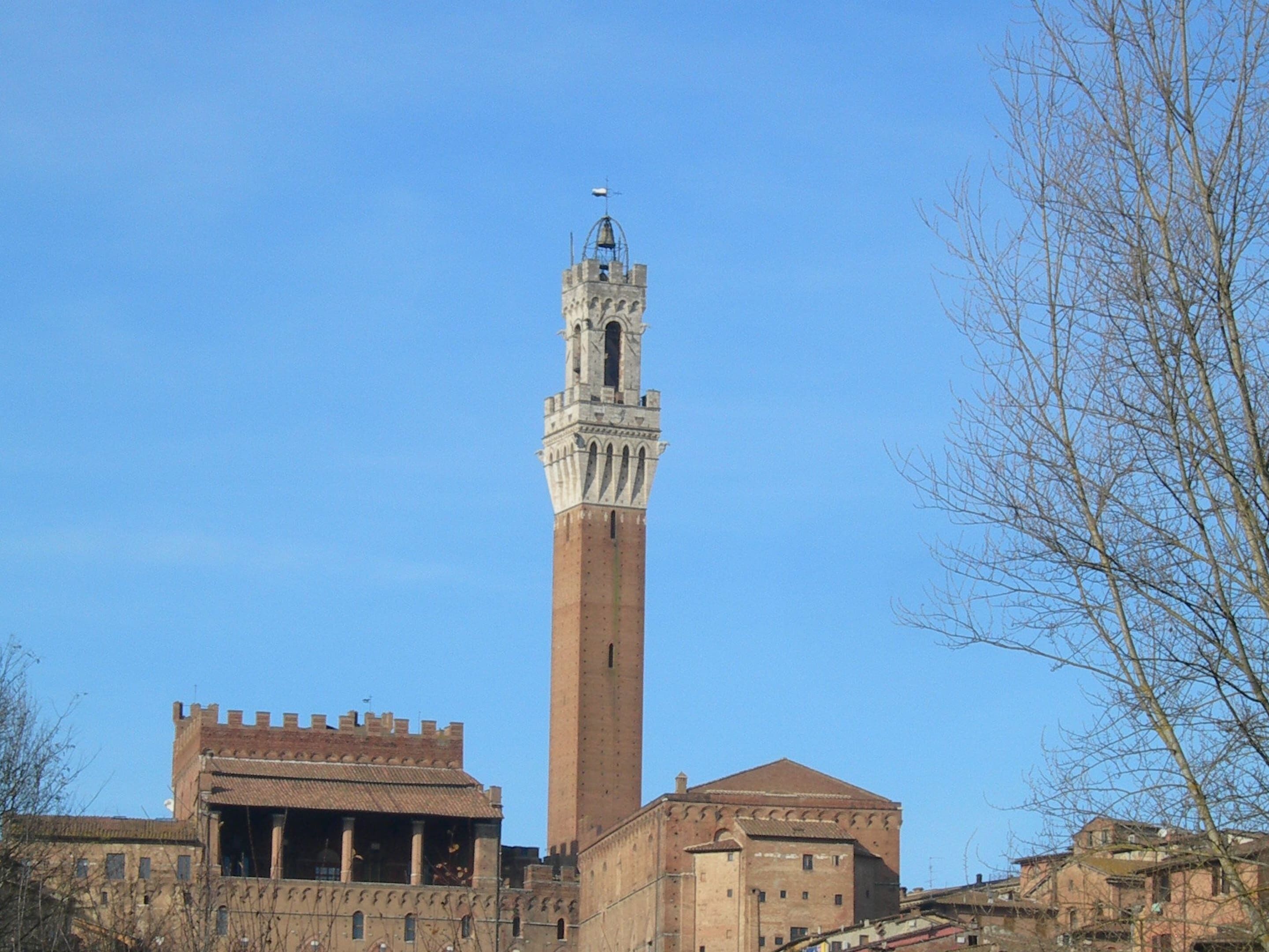 A tall tower with a clock and a flag, surrounded by historic buildings.