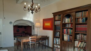 A dining area with a wooden table and chairs, a chandelier, a bookshelf filled with books, and a tiled floor. - Cozy 2-bedroom Apartment (Castelnuovo di Val di Cecina)