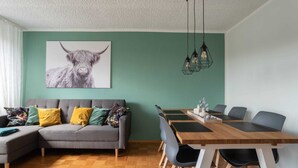 A modern living room with a grey sofa, a dining table with chairs, and a green wall. - Tranquil Apartment in Marktleuthen near River & Forest (Marktleuthen)