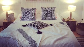 A bed with patterned pillows and a white blanket, two bedside lamps, and a decorative wall hanging. - Group Escape in Vielsalm (Vielsalm)