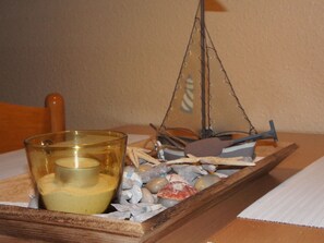 Ein Glaswindlicht mit einer Kerze auf einer Holztischplatte, übersät mit Kieselsteinen und Muscheln.