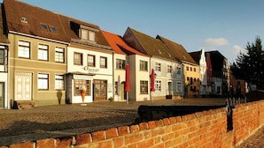 Una hilera de edificios tradicionales europeos, con una calle adoquinada y un muro de ladrillo en primer plano.