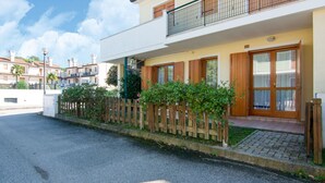 A two-story residential building with a wooden fence, a balcony, and a paved driveway. - Belvilla by OYO Holiday Home in Rosolina (Rosolina)