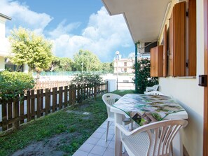 A patio with a table and chairs, a wooden fence, and a view of a residential area with trees and buildings. - Belvilla by OYO Holiday Home in Rosolina (Rosolina)