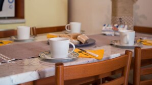 A dining table with white cups and saucers, a vase with flowers, and a wooden chair. - Belvilla by OYO Holiday Home in Rosolina (Rosolina)