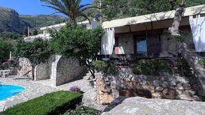 Un edificio de paredes de piedra con piscina, rodeado de vegetación y montañas.