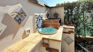 Un espacio exterior con suelo de baldosas, una piscina pequeña, una pared con azulejos decorativos y un farol colgante.