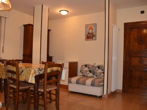 Ein Essbereich mit Holztischen und -stühlen, einer Couch mit gemusterten Kissen und einem Holzschrank.