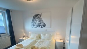 Habitación de hotel con una cama, dos mesitas de noche, una obra de arte con cebra en la pared y una ventana con cortinas.
