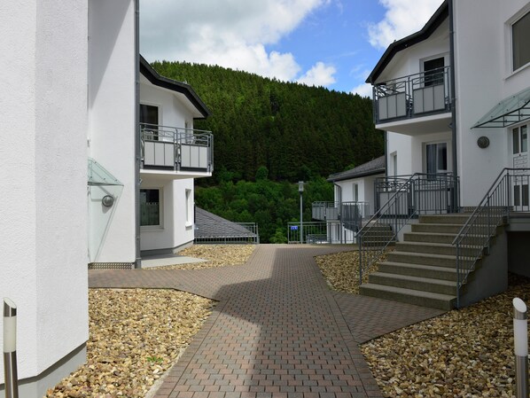 A modern building with a paved walkway, a staircase, and a view of a forested hill.