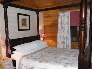 Un lit à baldaquin avec du linge de lit blanc et une couvre-lit à motifs floraux, une tête de lit en bois et un tableau encadré au mur.