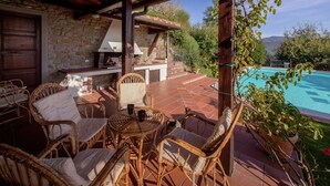 An outdoor patio with wicker furniture, a stone wall, and a view of a swimming pool. - Villa in Tuscany With Pool and Valley Views (Castiglion Fiorentino)