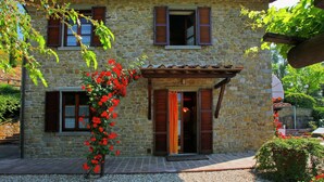 A stone house with a tiled roof, wooden shutters, and a gravel driveway. - Villa in Tuscany With Pool and Valley Views (Castiglion Fiorentino)