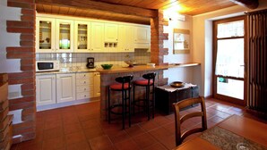 A kitchen with white cabinets, a brick accent wall, a wooden ceiling, and a window with curtains. - Villa in Tuscany With Pool and Valley Views (Castiglion Fiorentino)