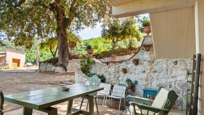 An outdoor patio with a stone wall, a wooden table, and white chairs. - Apartment in Stroncone Near Piediluco Lake (Stroncone)