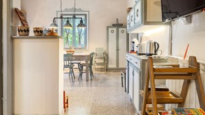 A kitchen with a dining area, wooden cabinets, a television, and a window with curtains. - Apartment in Stroncone Near Piediluco Lake (Stroncone)