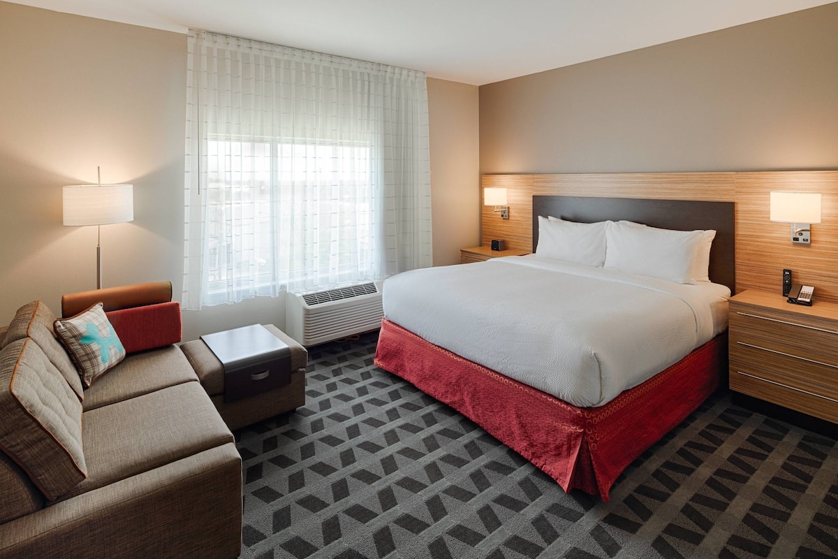 A hotel room with a large bed, a sofa, a desk, and a window with curtains.