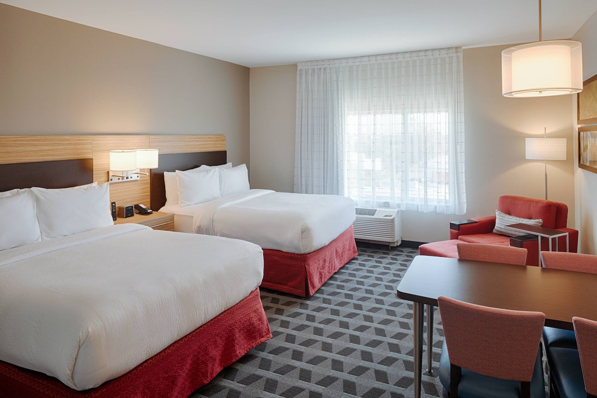 A hotel room with two beds, a desk, a chair, and a large window with curtains.