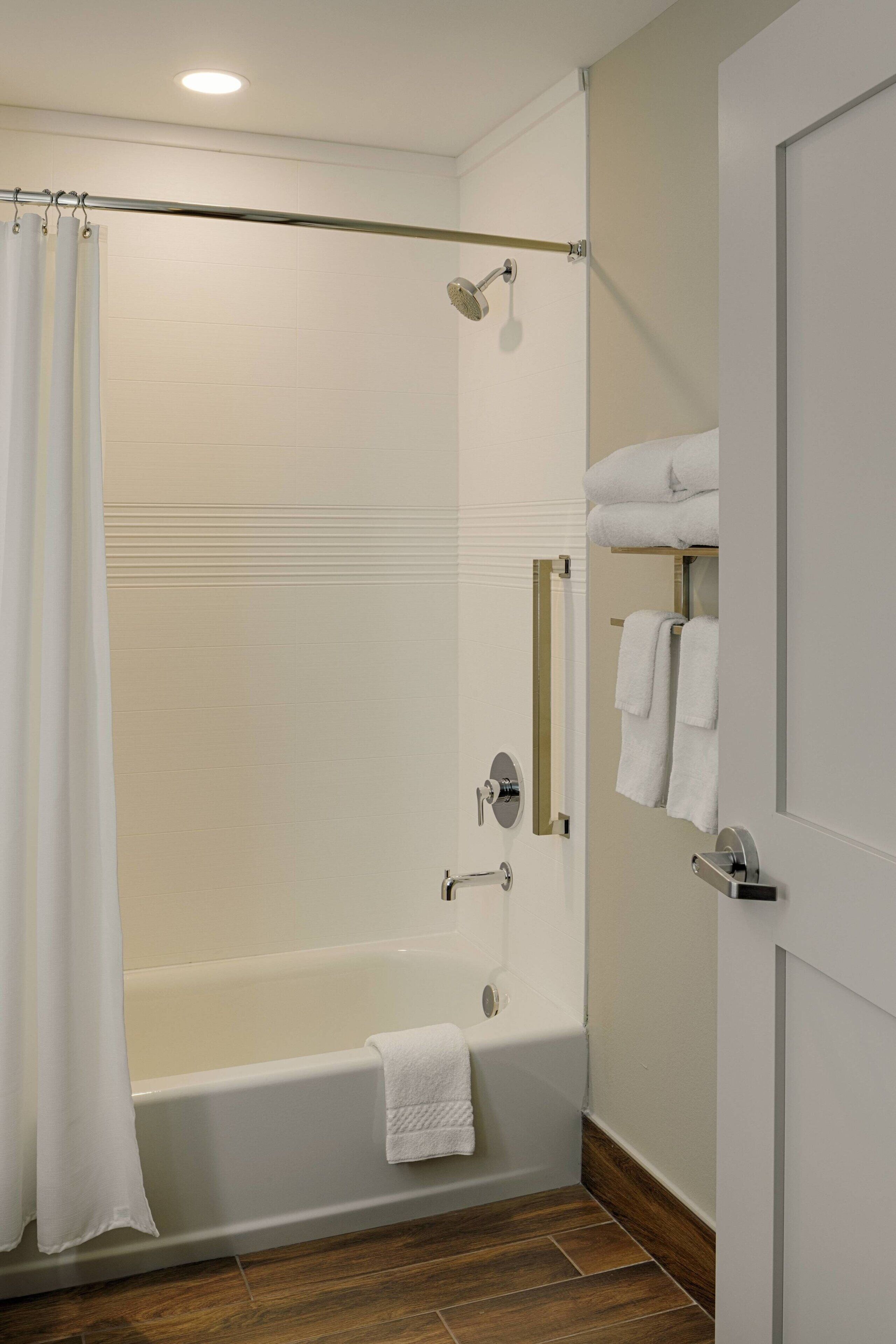 A modern bathroom with a bathtub, shower, and a towel rack.