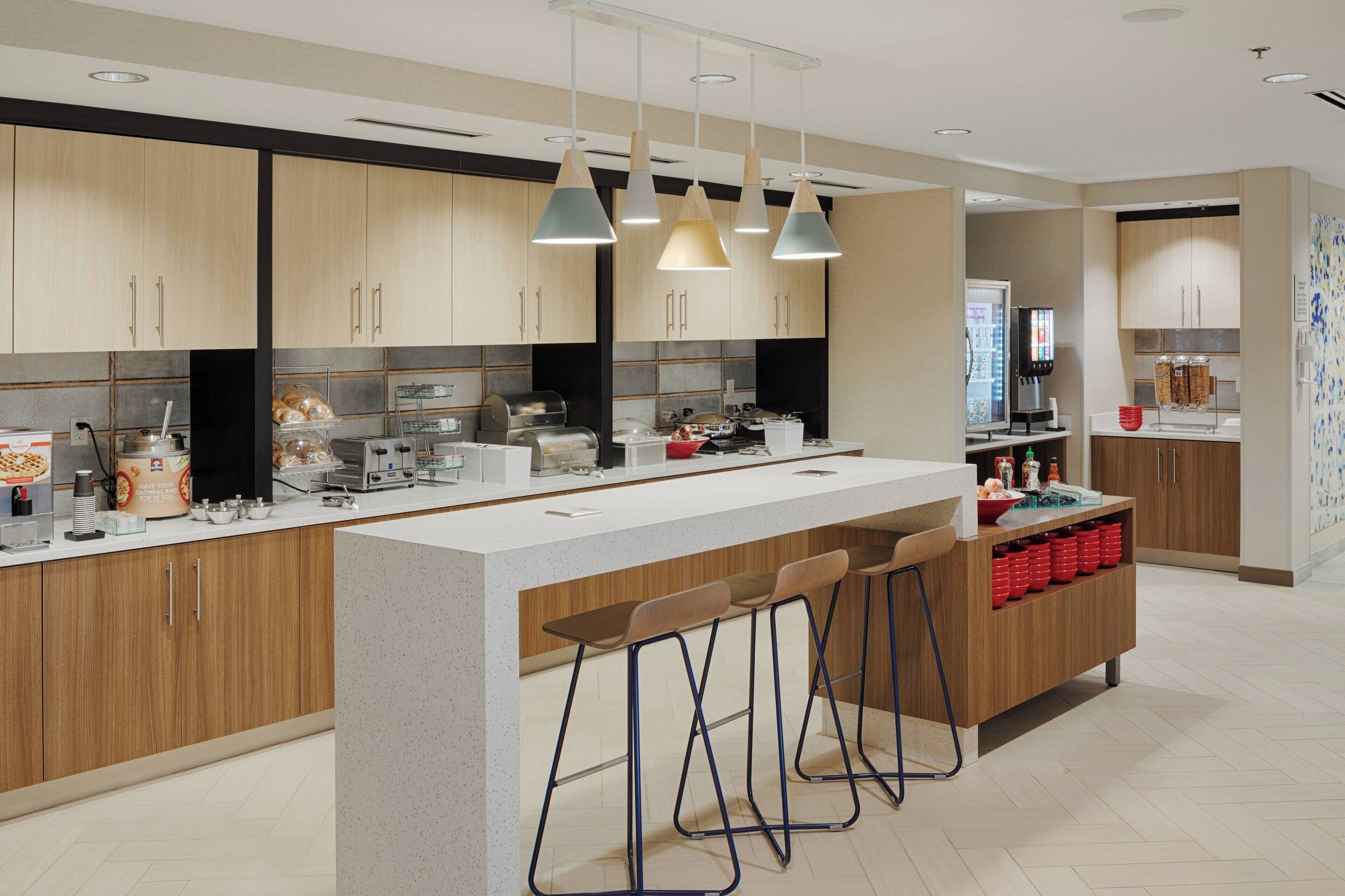 Una cocina moderna con armarios de madera, una isla central con taburetes de bar e iluminación colgante.