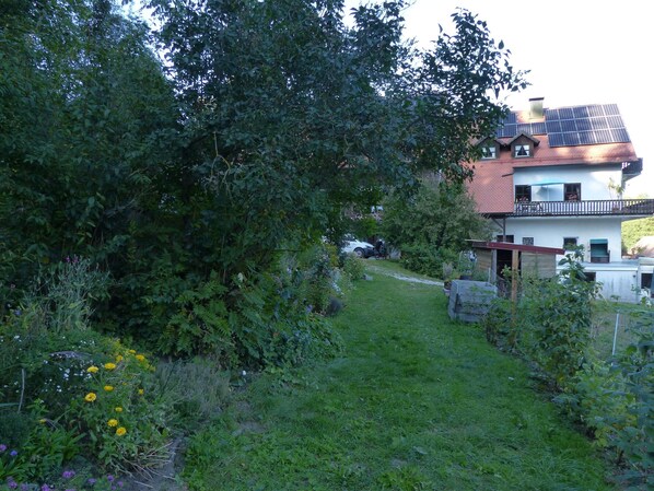 A house with solar panels, a garden with various plants and flowers, and a car parked in the driveway.