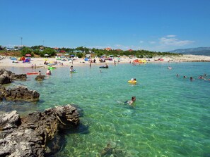 Ein Strand mit klarem Wasser, Felsen und Menschen, die schwimmen und sich sonnen.