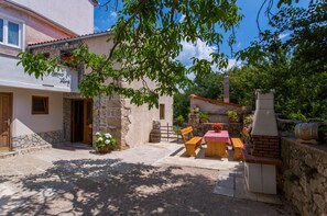 A rustic stone building with a stone staircase leading to a wooden door. There is a wooden bench and table set up outside, with a brick oven and barrels nearby. - Holiday Home in Polje Near Beach (Dobrinj)
