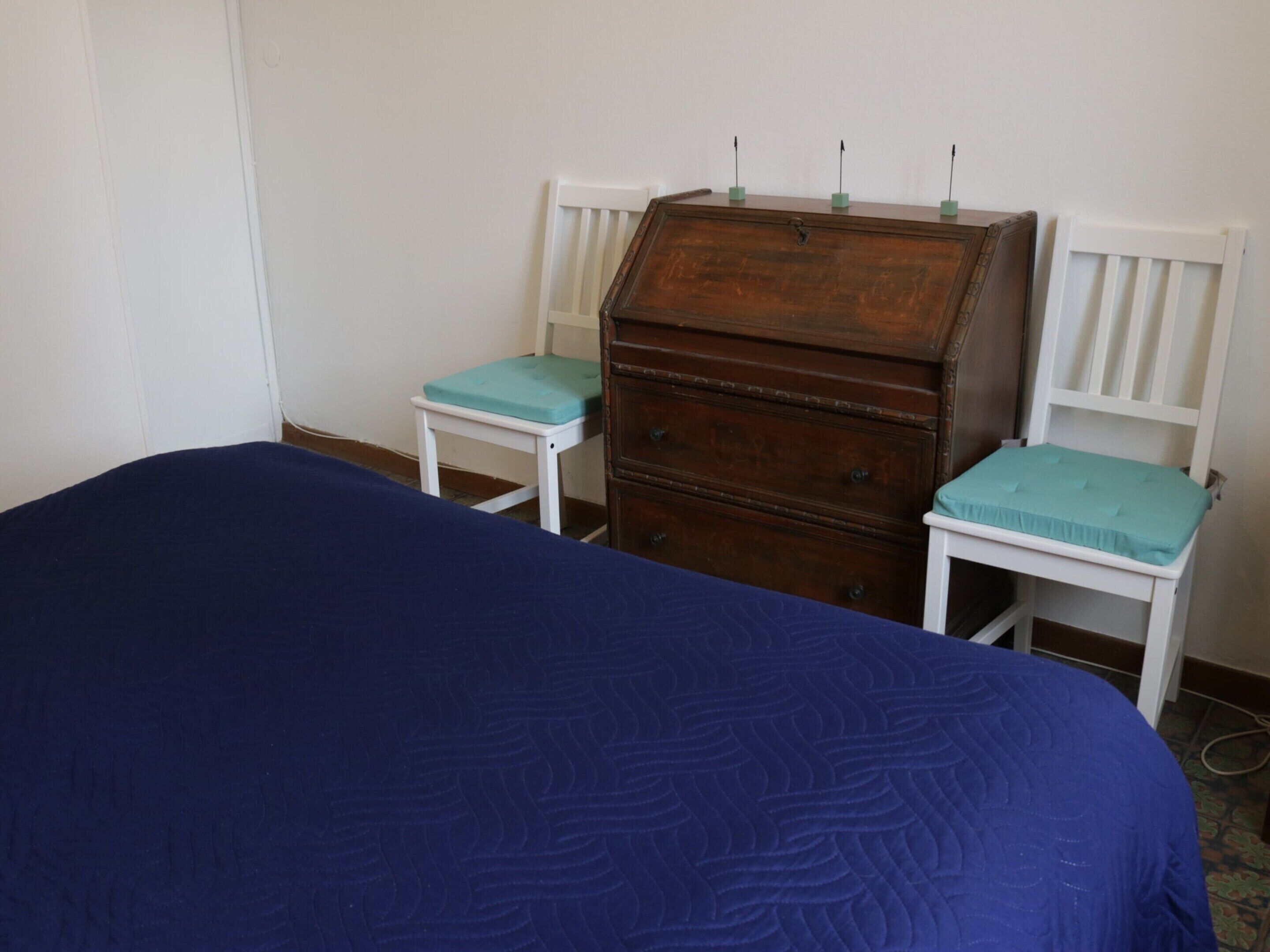 A bedroom with a bed, a wooden dresser, and two chairs.