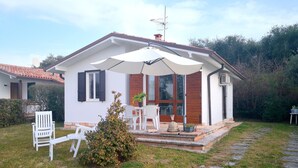 Una casa con un patio, sillas blancas, una mesita y una planta en maceta.