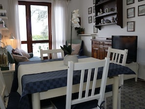 Um quarto com uma mesa de jantar, cadeiras, uma televisão, uma estante de livros e uma janela com cortinas.