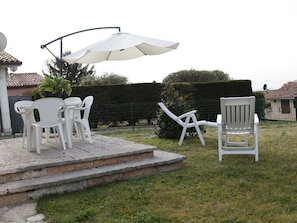 Uma área de pátio com mesa, cadeiras, um guarda-sol branco e uma cadeira branca.