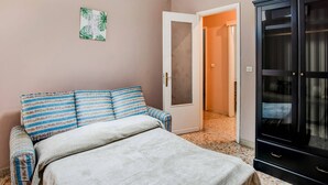 A bedroom with a bed, a wardrobe, a door leading to another room, and a wall with a framed picture.
